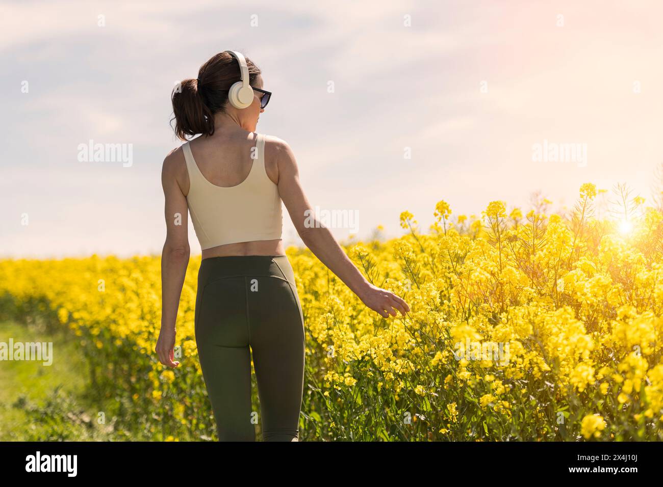 Sporty woman walking in the countryside through a yellow field, rear view. Stock Photo