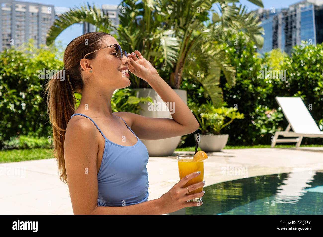 A woman is putting on sunglasses beside the swimming pool Stock Photo