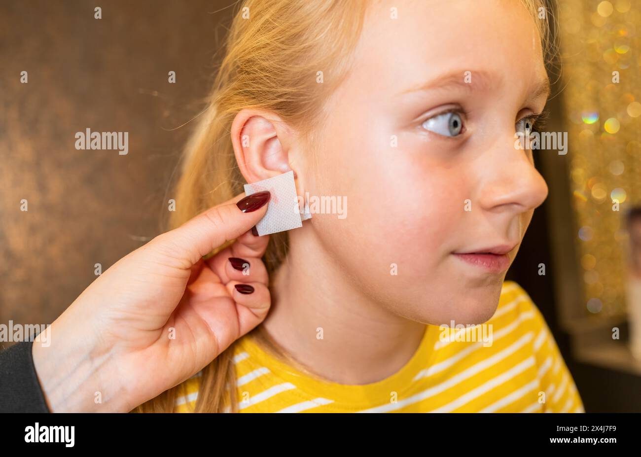hand applying a disinfectant wipe to a young girl's earlobe bdefore ear piercing in a beauty