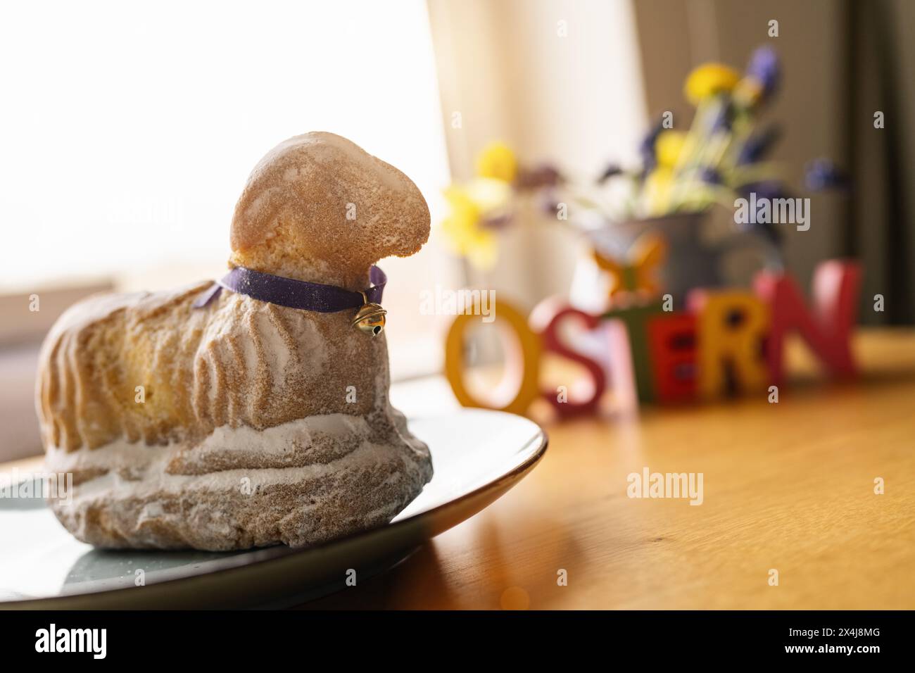 Lamb-shaped Easter cake with purple ribbon on a wooden table with flowers and the blurred  german word  'Ostern' in english easter Stock Photo