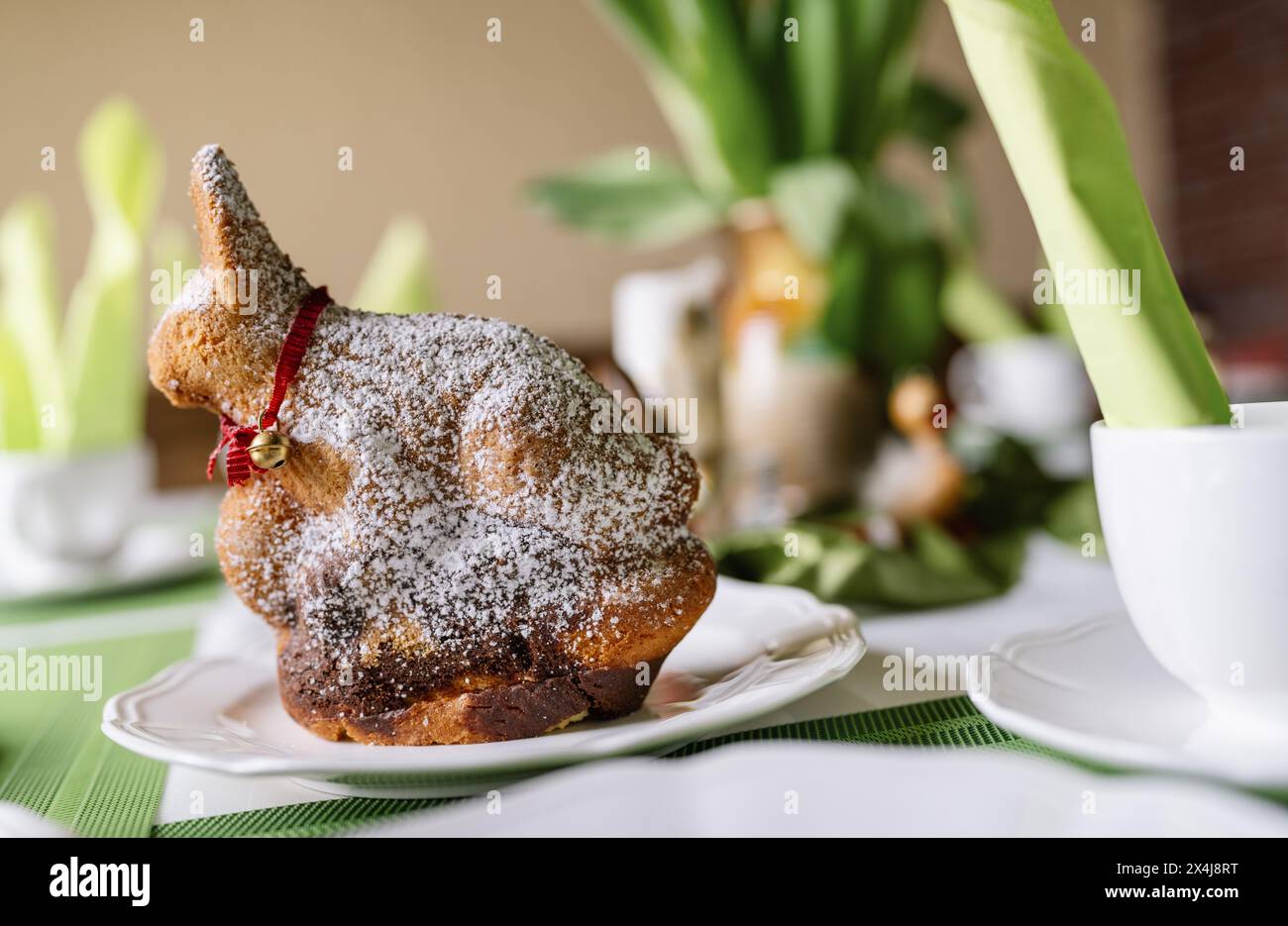 Easter cake in a bunny shape with powdered sugar on a festive table with green accents. Stock Photo