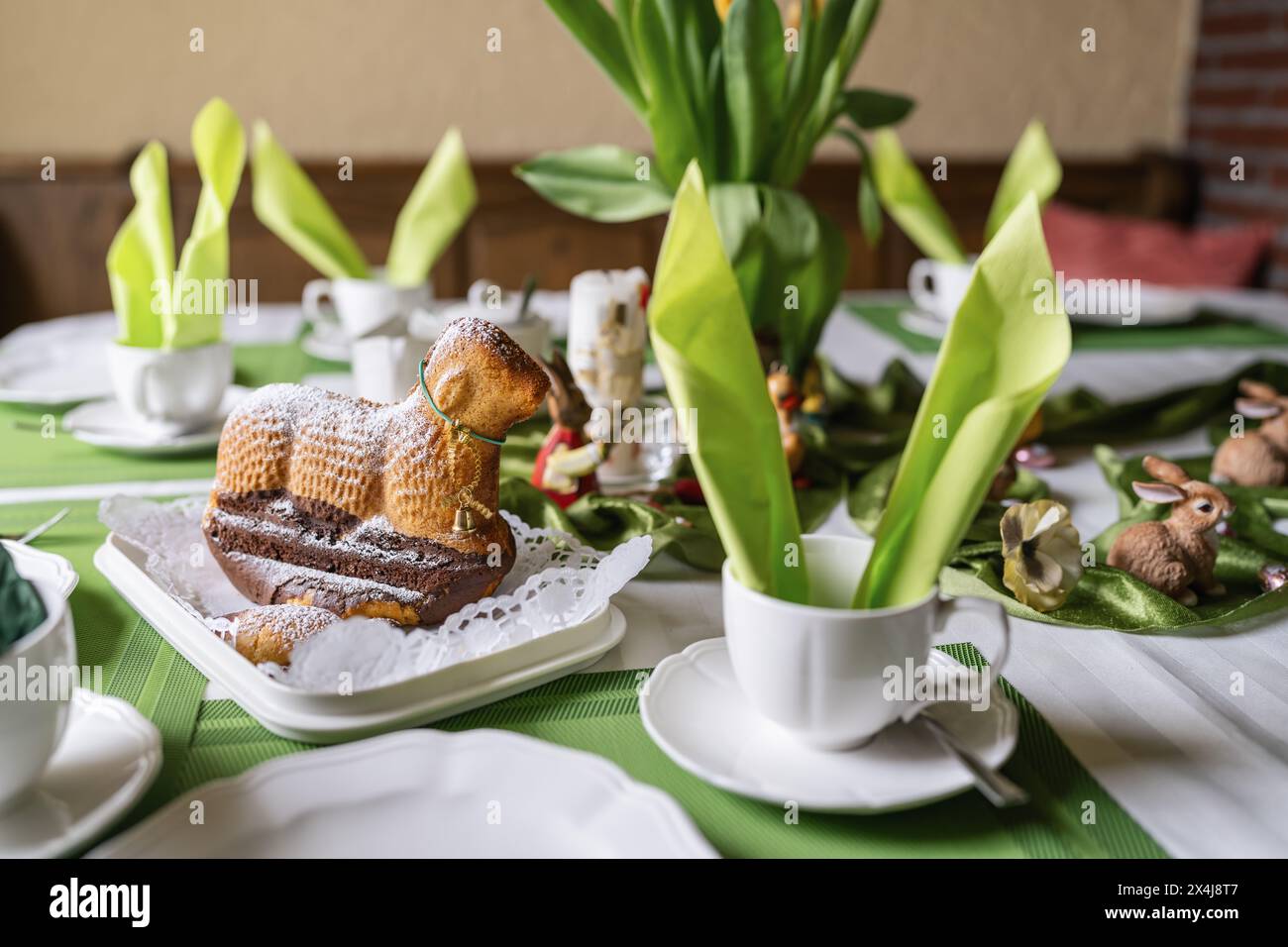 Easter-themed table setting with cake lamb dusted with powdered sugar, tulips, and decorations Stock Photo
