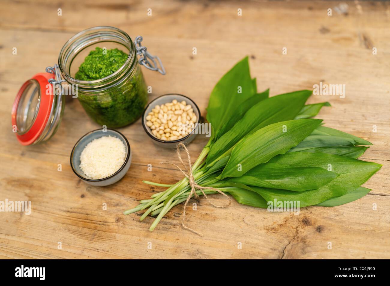 Wild garlic pesto in jar with pine nuts, grated Parmesan cheese, and fresh leaves on wood Stock Photo