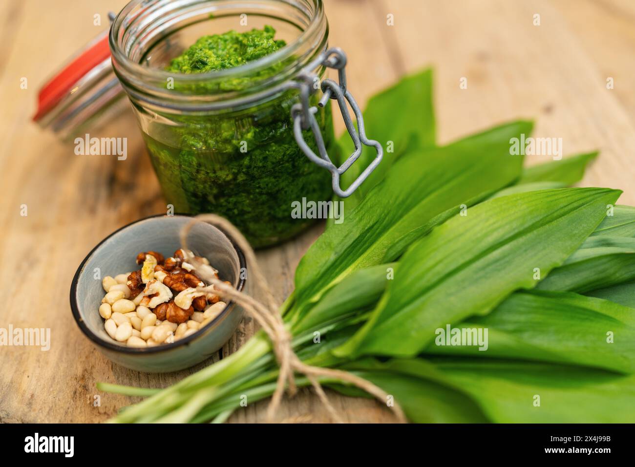 Jar of wild garlic pesto with pine nuts, walnuts, and fresh leaves on a wooden table Stock Photo