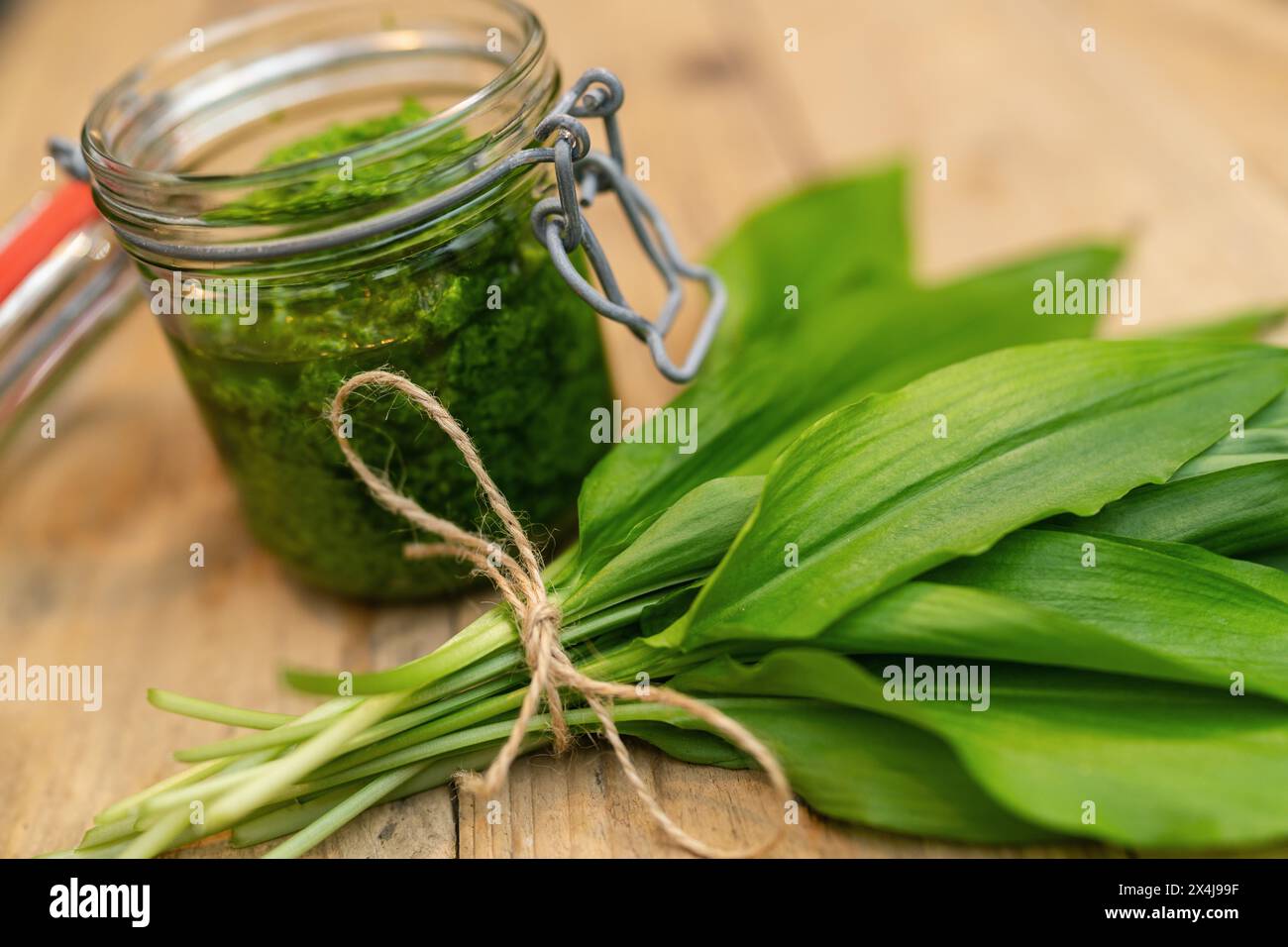 Close-up of wild garlic pesto in an open glass jar with fresh leaves on a wooden surface Stock Photo