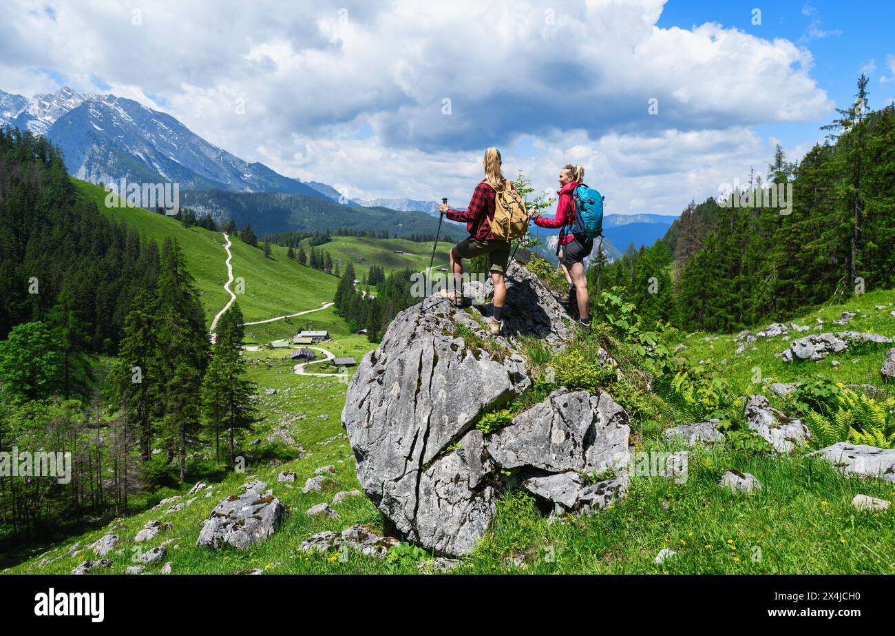 Two female hikers with backpacks standing on a rock and looking in to the valley at the mountains in bavarian alps Stock Photo