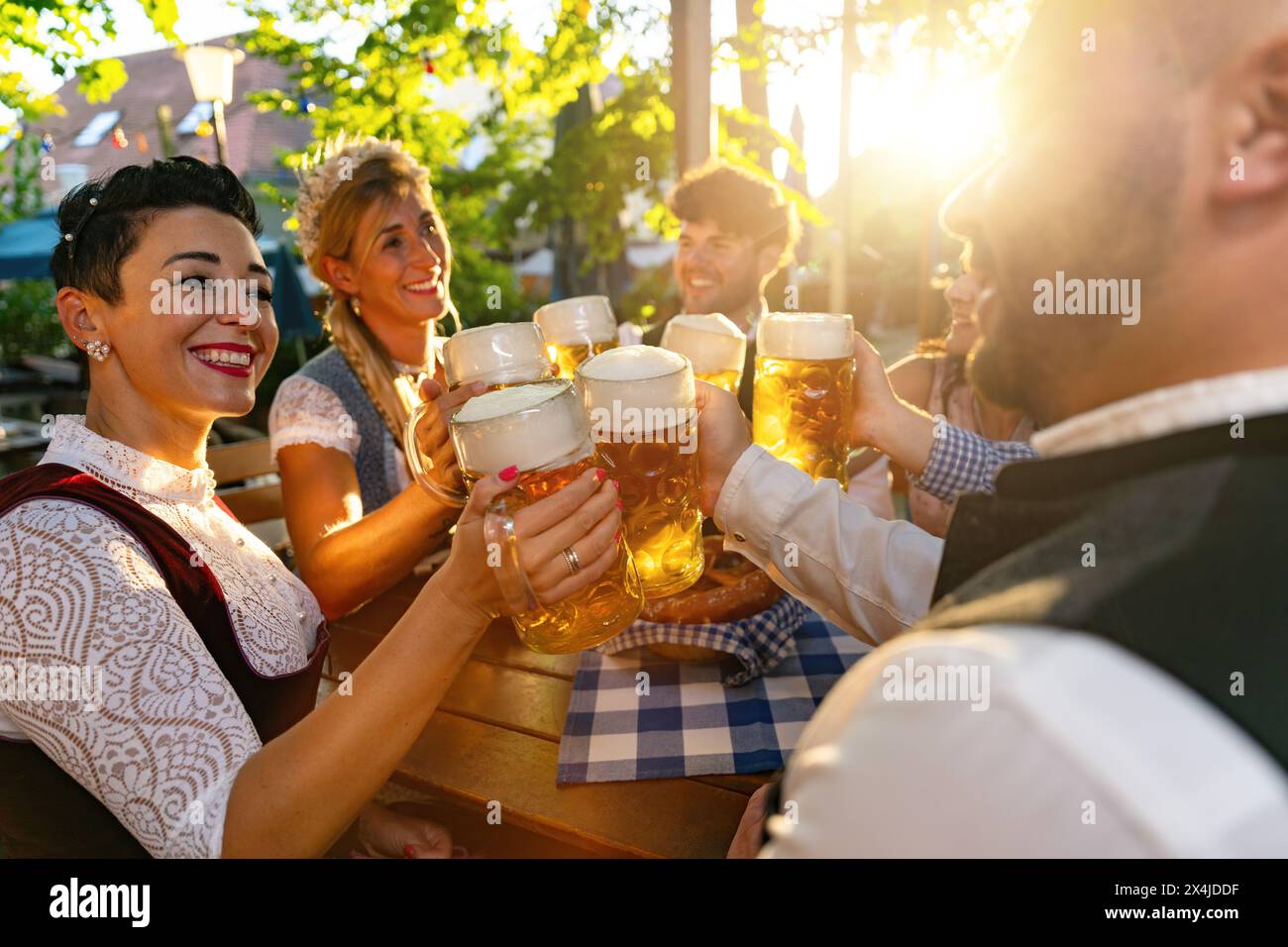 Group of friends clinking beer mugs in traditional beer garden or oktoberfest in Bavaria, Germany, at sunset Stock Photo