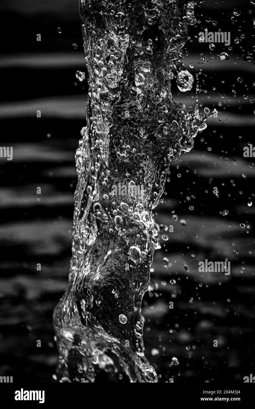 Droplets suspended from a jet of water from a fountain - Dark black and white background Stock Photo