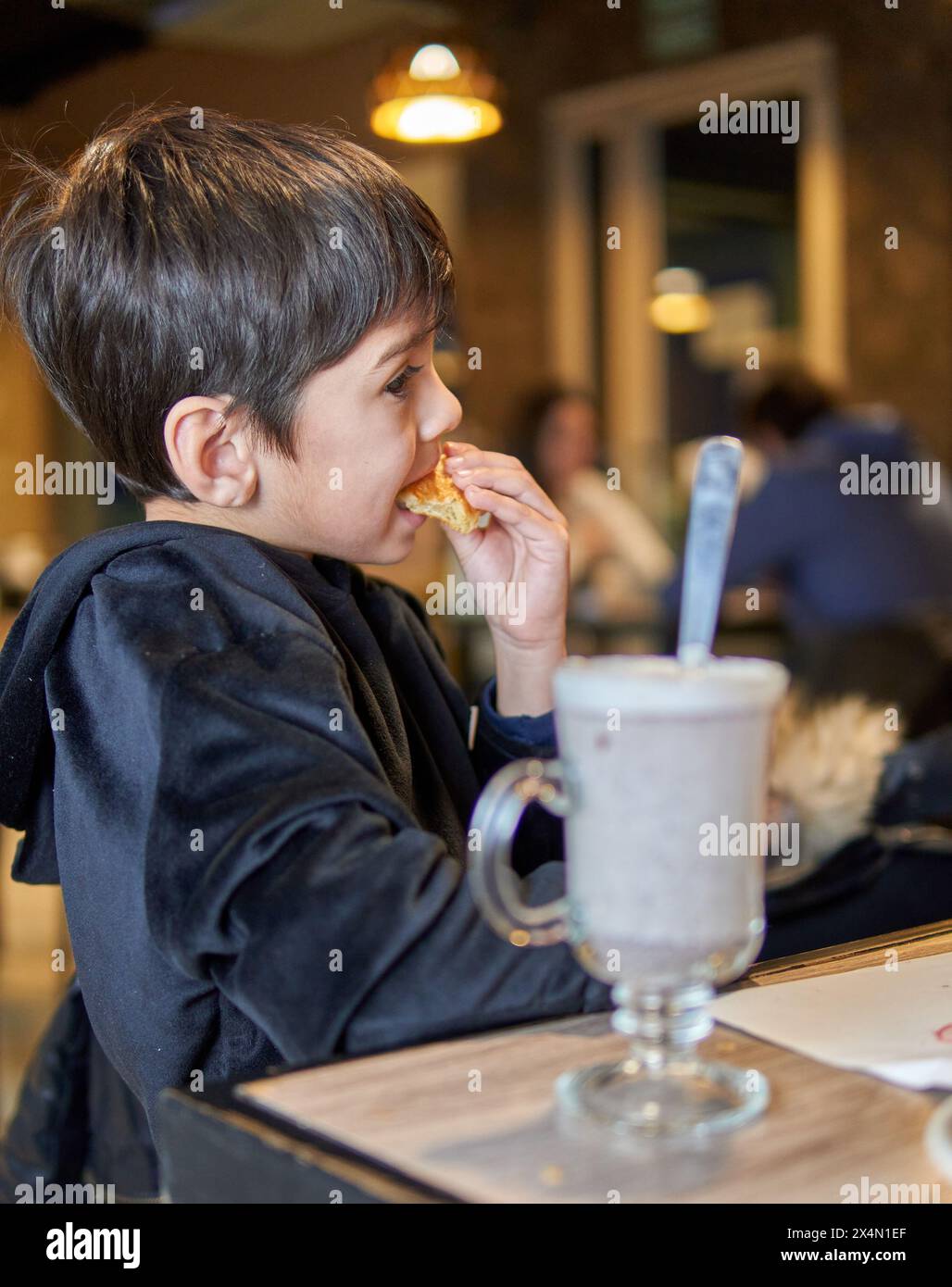 Latino child snacking on a croissant and a chocolate milk at a bar in Argentina. Stock Photo