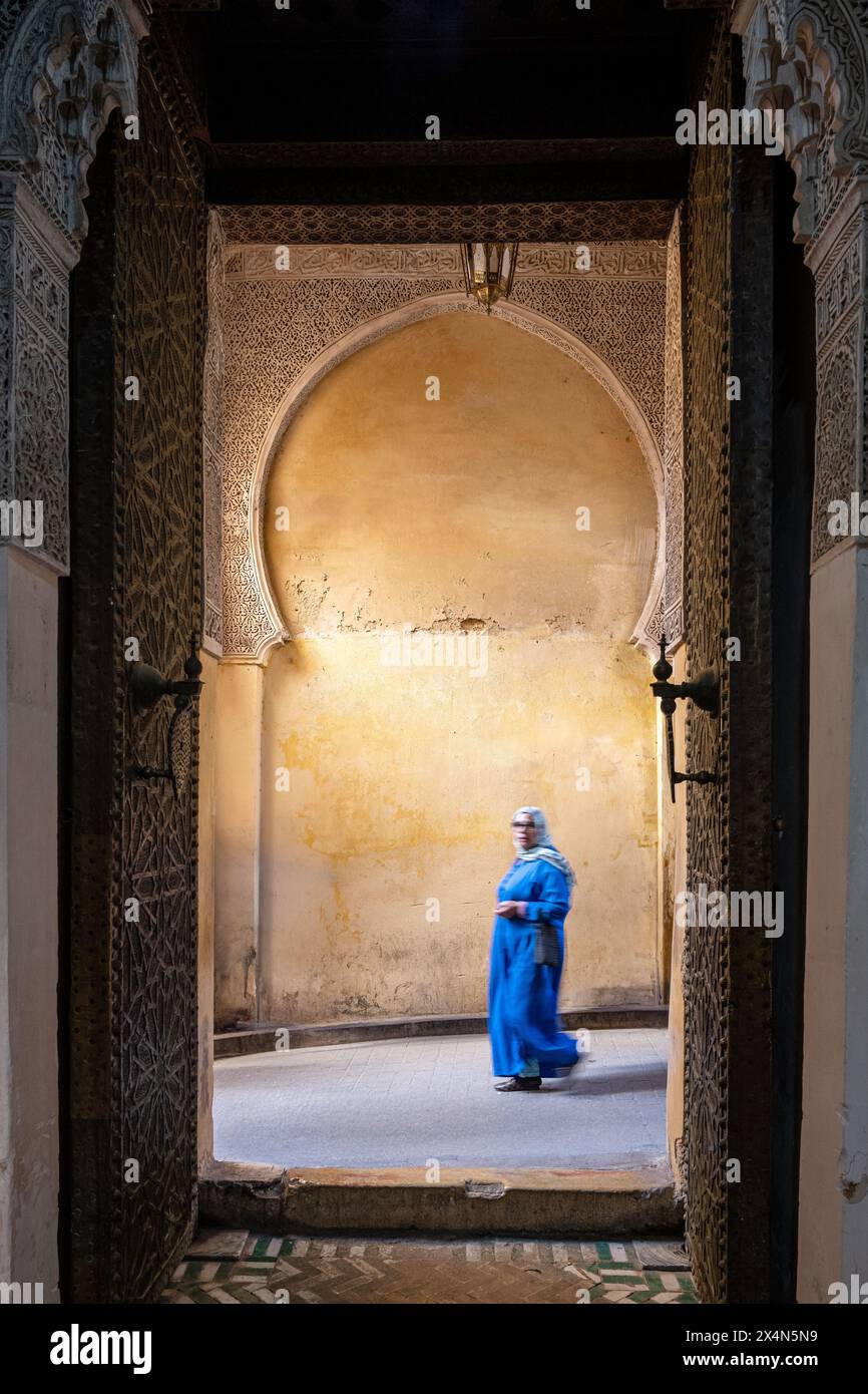 A woman in blue walks through the ornate gateway of Cherratine Madrasa