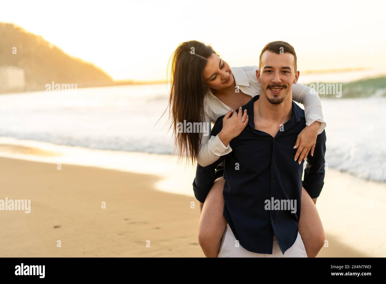 Woman piggybacking her boyfriend on the beach during sunset Stock Photo