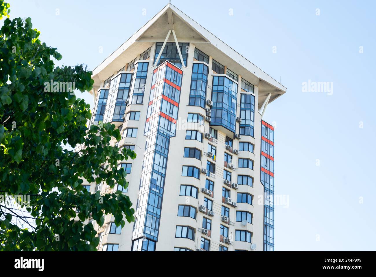 super modern residential high-rise building with green tree on blue sky background. Stock Photo