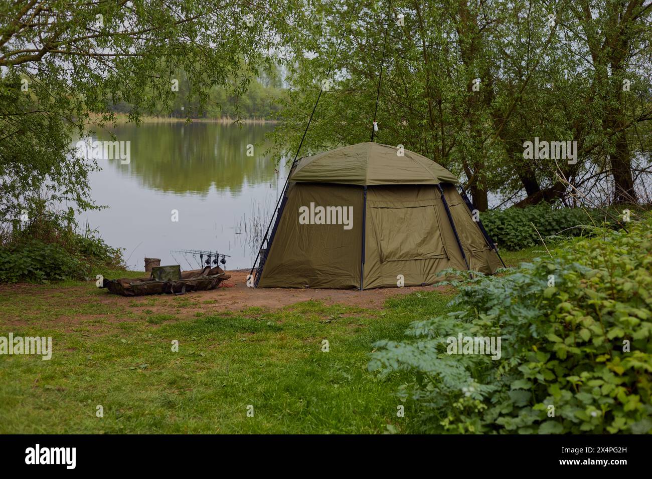 Landscape image of a lake and surrounding trees with a fisherman's shelter and equipment in the fore ground. Stock Photo