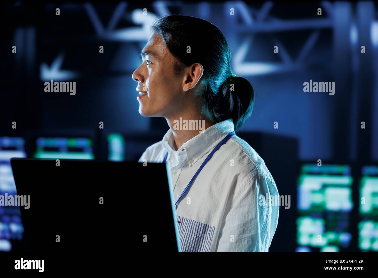 Cheerful BIPOC man between server hub rows providing processing resources for businesses worldwide. Computer scientist fixing data center mainframes tasked with managing massive databases Stock Photo
