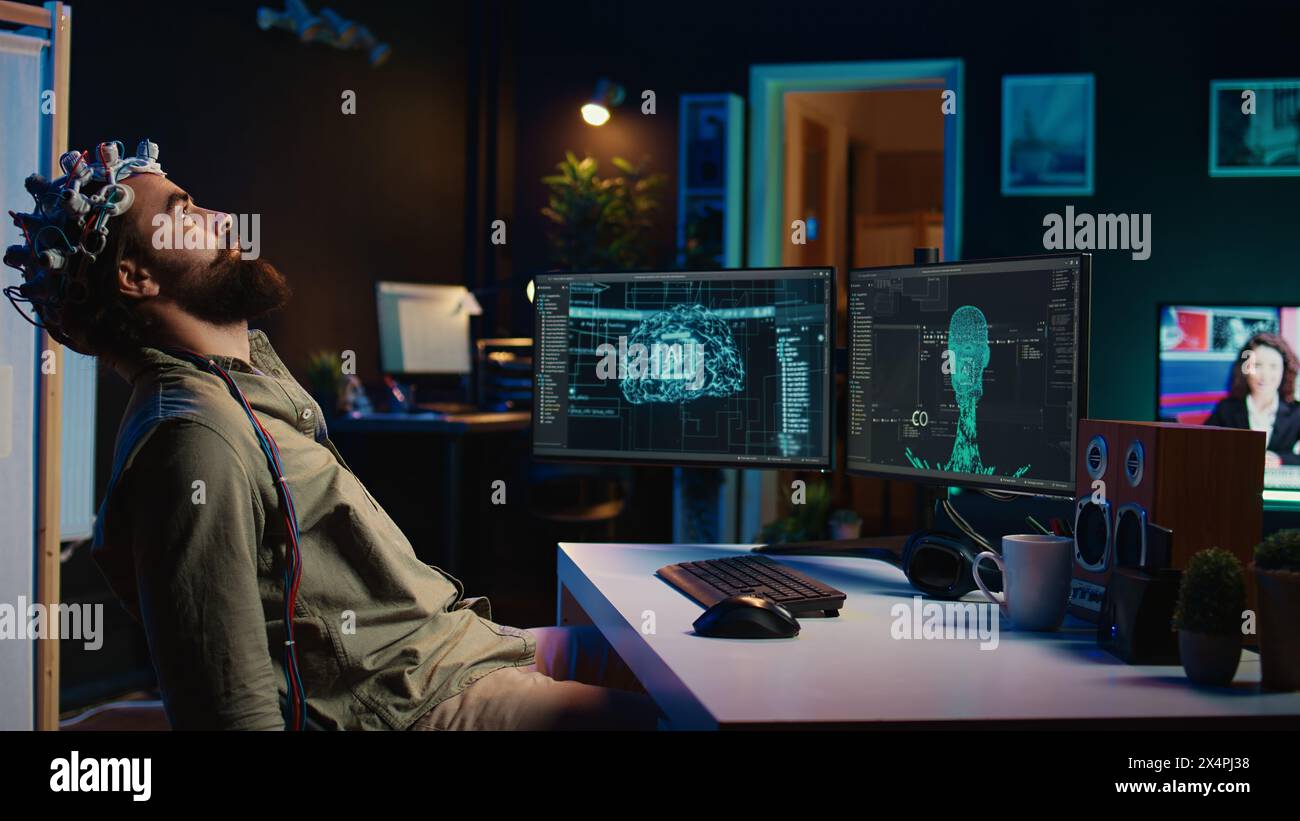 Programmer using EEG headset to upload his mind into computer, attaining immortality. Neuroscientist experimenting with transferring consciousness into cyberspace, camera B Stock Photo