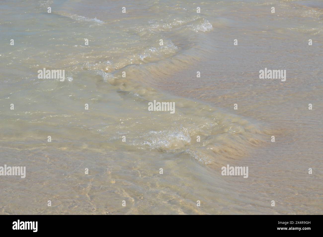 At Ponce Inlet Beach, Florida, the ocean's edge sends water rushing over the sand, creating herringbone-patterned, washed-out ripples. Stock Photo