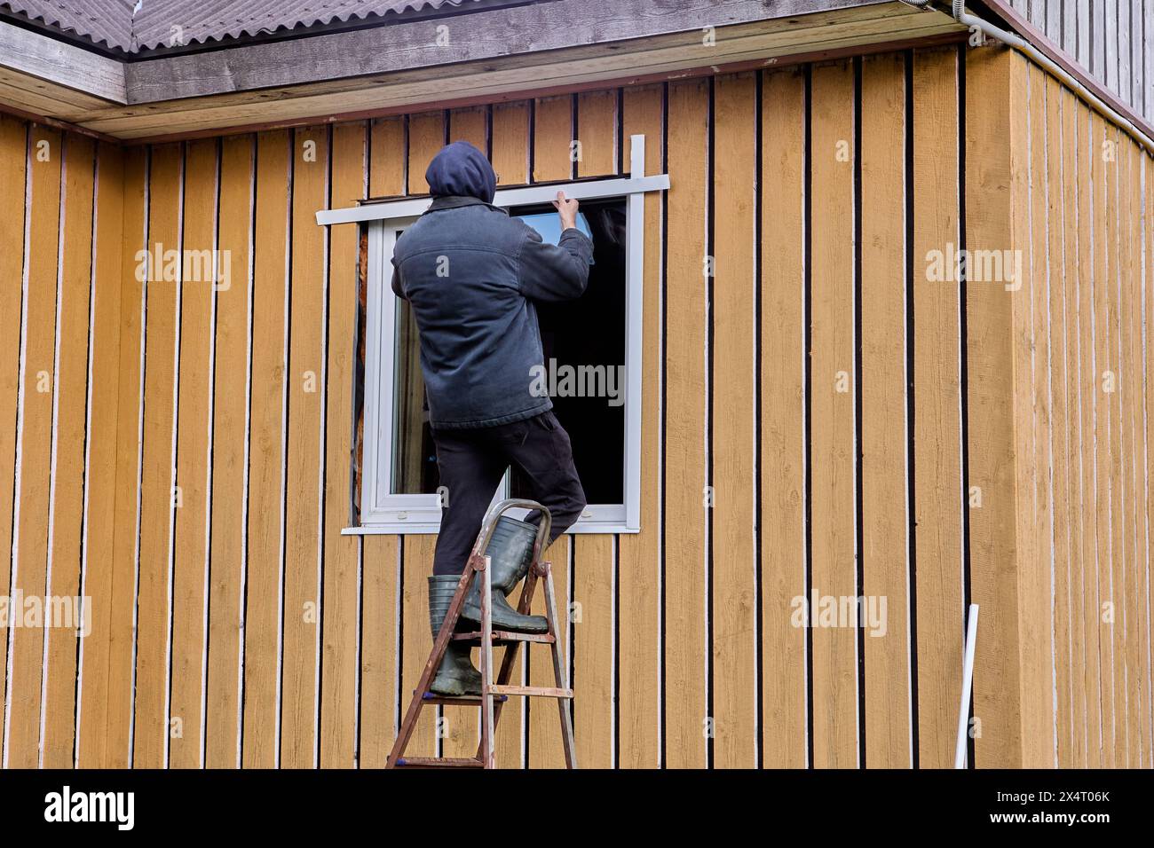 Installation of external metal slopes on window of wooden rural house, outdoor work of construction worker. Stock Photo