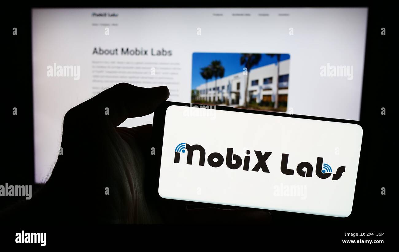 Person holding smartphone with logo of US fabless semiconductor company Mobix Labs Inc. in front of website. Focus on phone display. Stock Photo