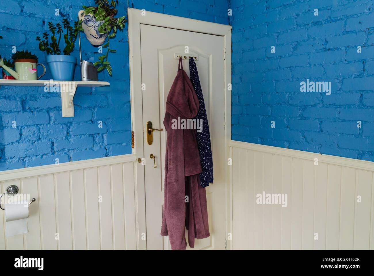 Isolated bathroom door with robes and pyjamas hanging on it and a shelf to the side Stock Photo