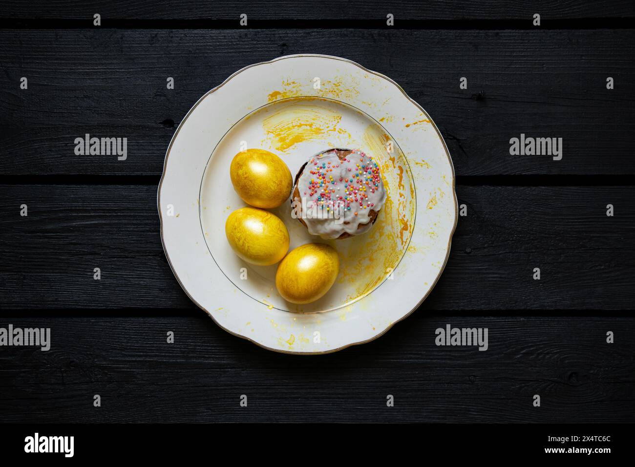 Homemade Easter cake and golden colored eggs stand on a plate on a black board, Easter holiday in Ukraine Stock Photo