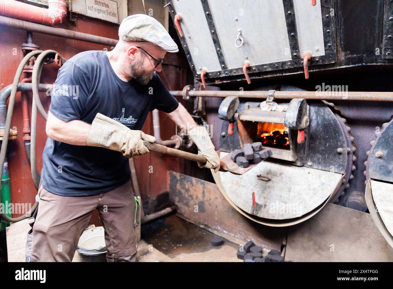 Berlin, Germany. 05th May, 2024. Stephan Hässelbarth, boiler attendant and stoker, shovels coal in the boiler room of steam tug Andreas before departure from the Historic Port of Berlin. The start of the season traditionally begins with a first round trip from the Historic Port. Credit: Christoph Soeder/dpa/Alamy Live News Stock Photo