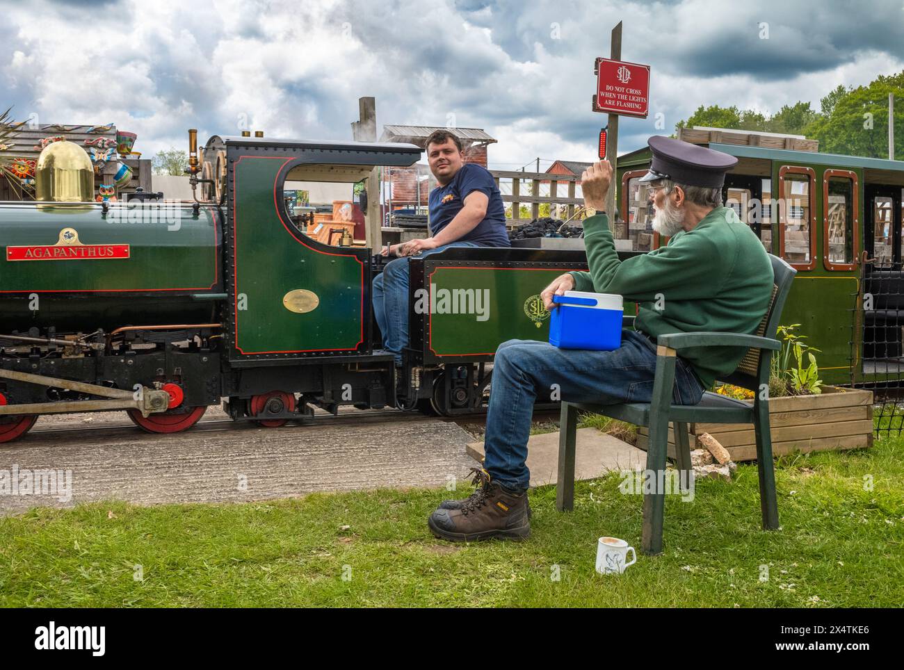 A volunteer drives The Railway Mission minature steam locomotive past a guard  at South Downs Light Railway, Pulborough, UK Stock Photo