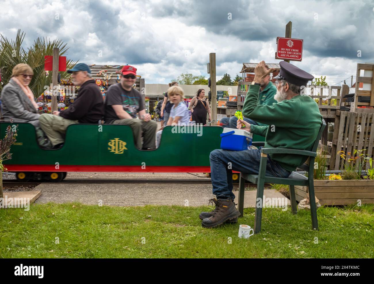 A volunteer guard waves at passengers on the The Railway Mission minature steam locomotive and carriages at South Downs Light Railway, Pulborough, UK Stock Photo