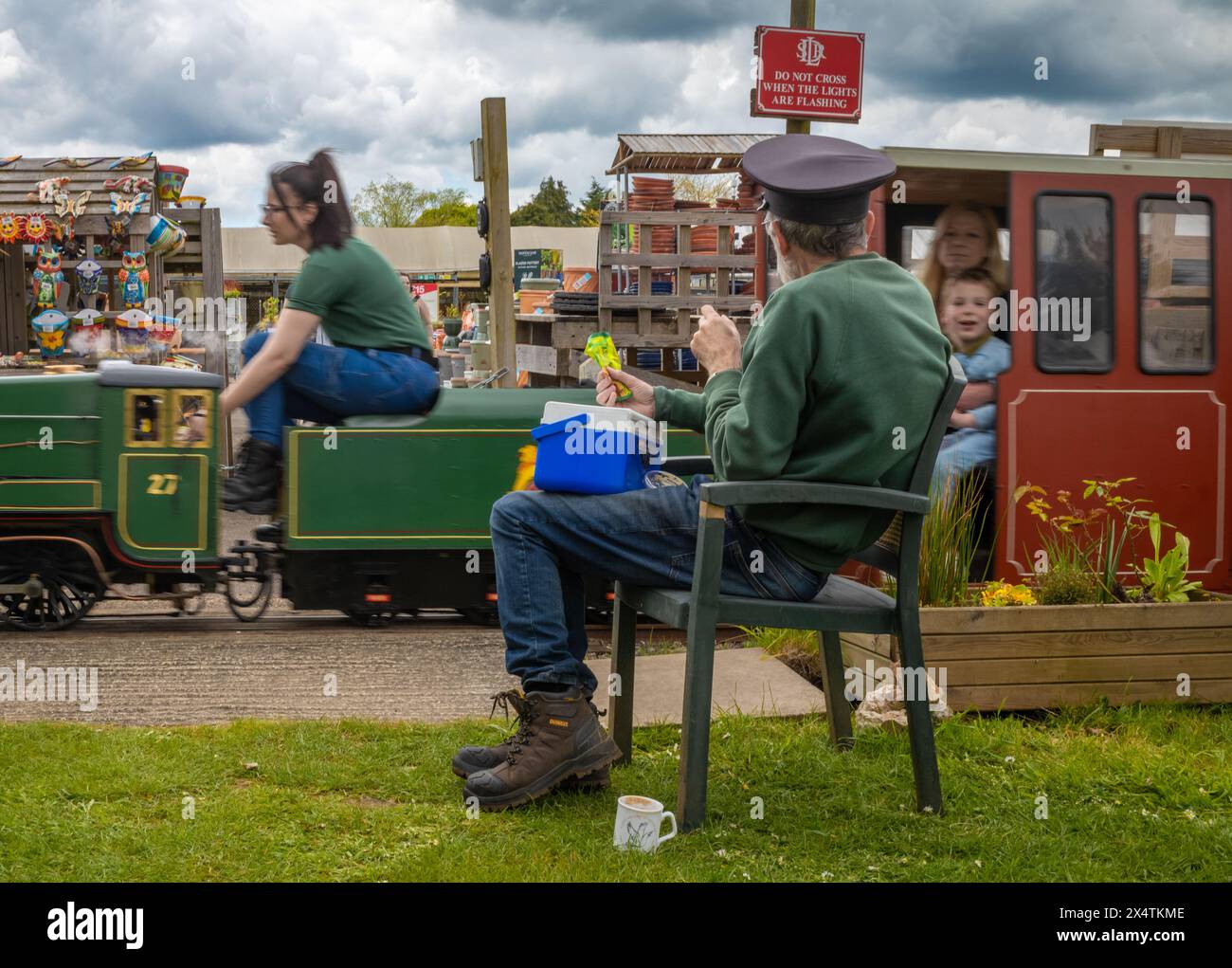 A volunteer drives The Railway Mission minature steam locomotive and its passengers passed a volunteer guard South Downs Light Railway, Pulborough, UK Stock Photo