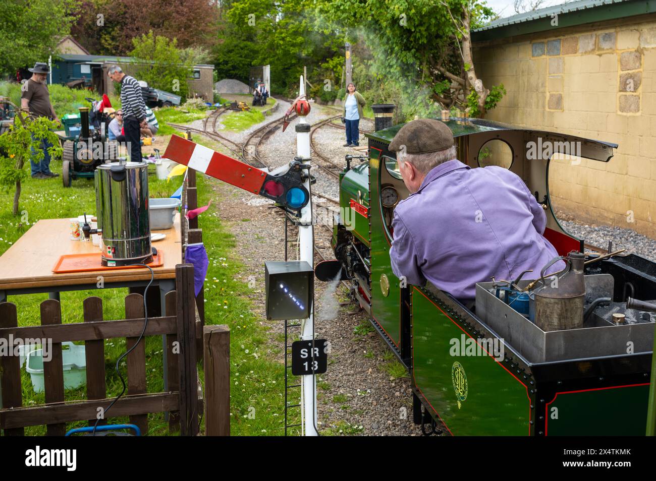 A volunteer drives Agapanthus, a miniature steam locomotive and its carriages, past a signal at South Downs Light Railway, Pulborough, UK. Stock Photo