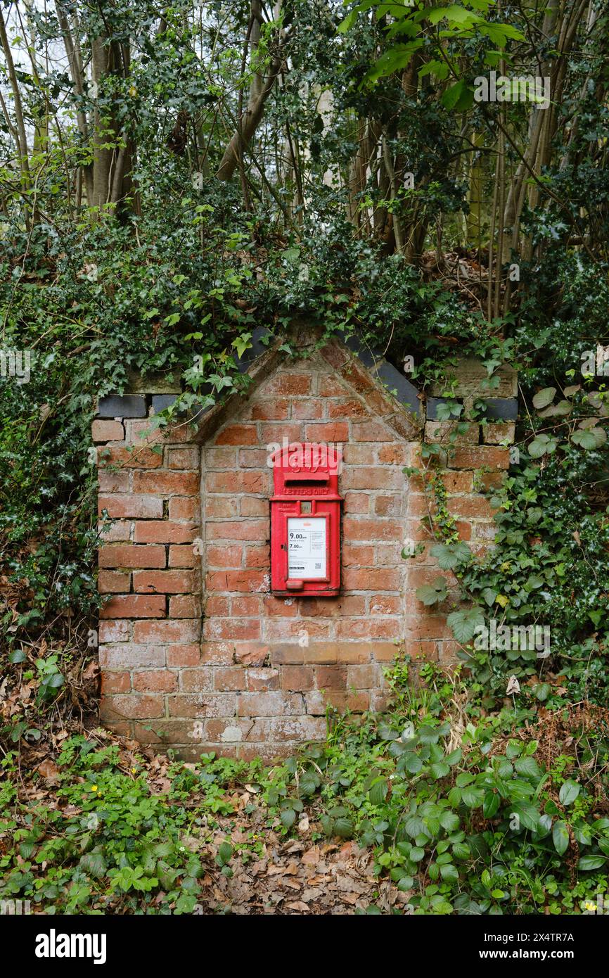 Red letter box in a brick wall by a country lane in England Stock Photo