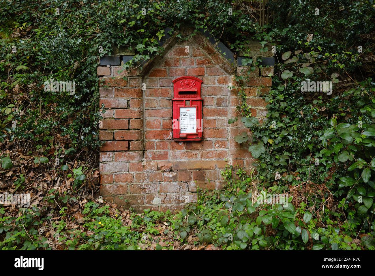 Red letter box in a brick wall by a country lane in England Stock Photo