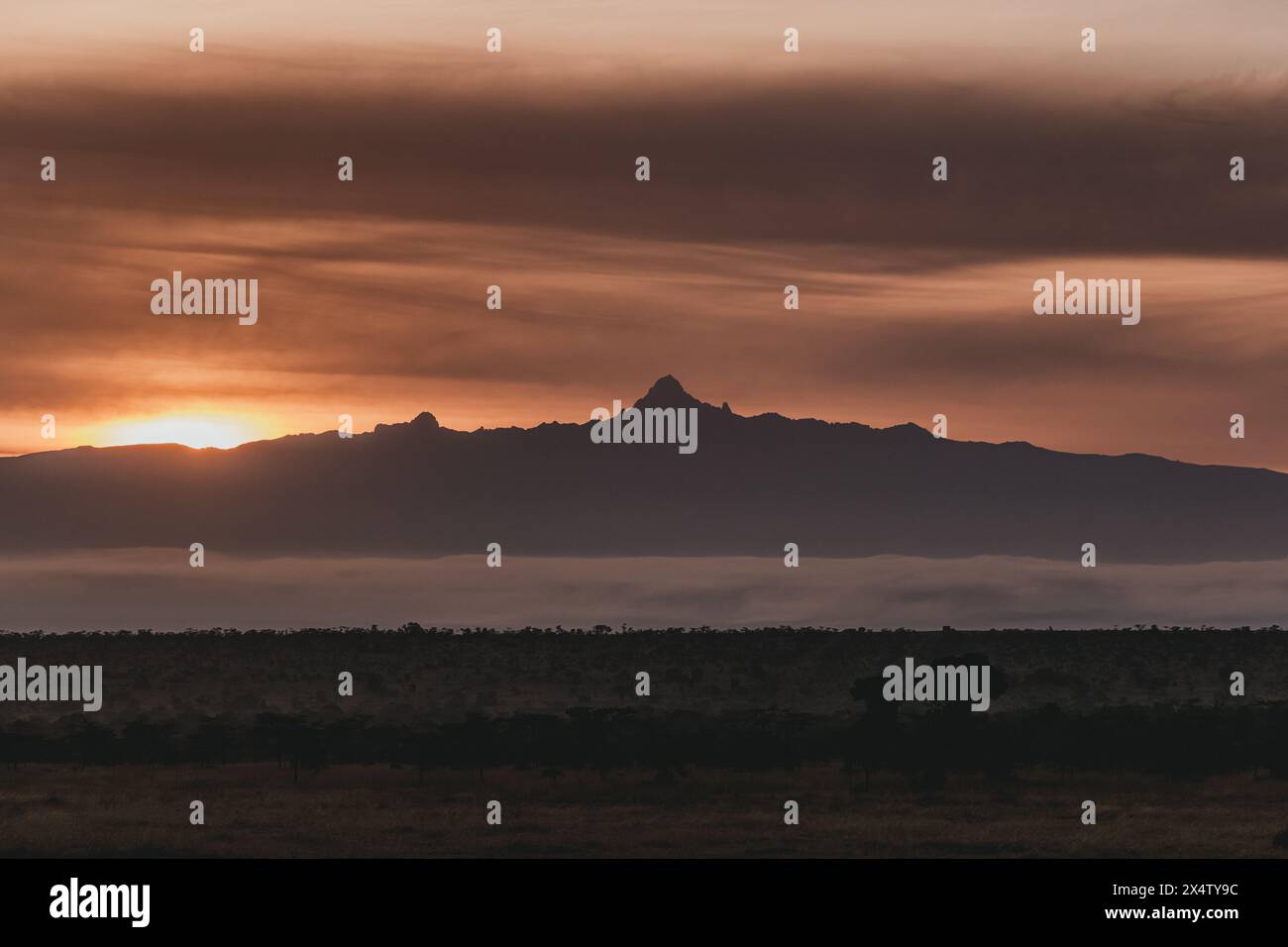 Fiery sunset silhouettes Mount Kenya over misty landscape Stock Photo