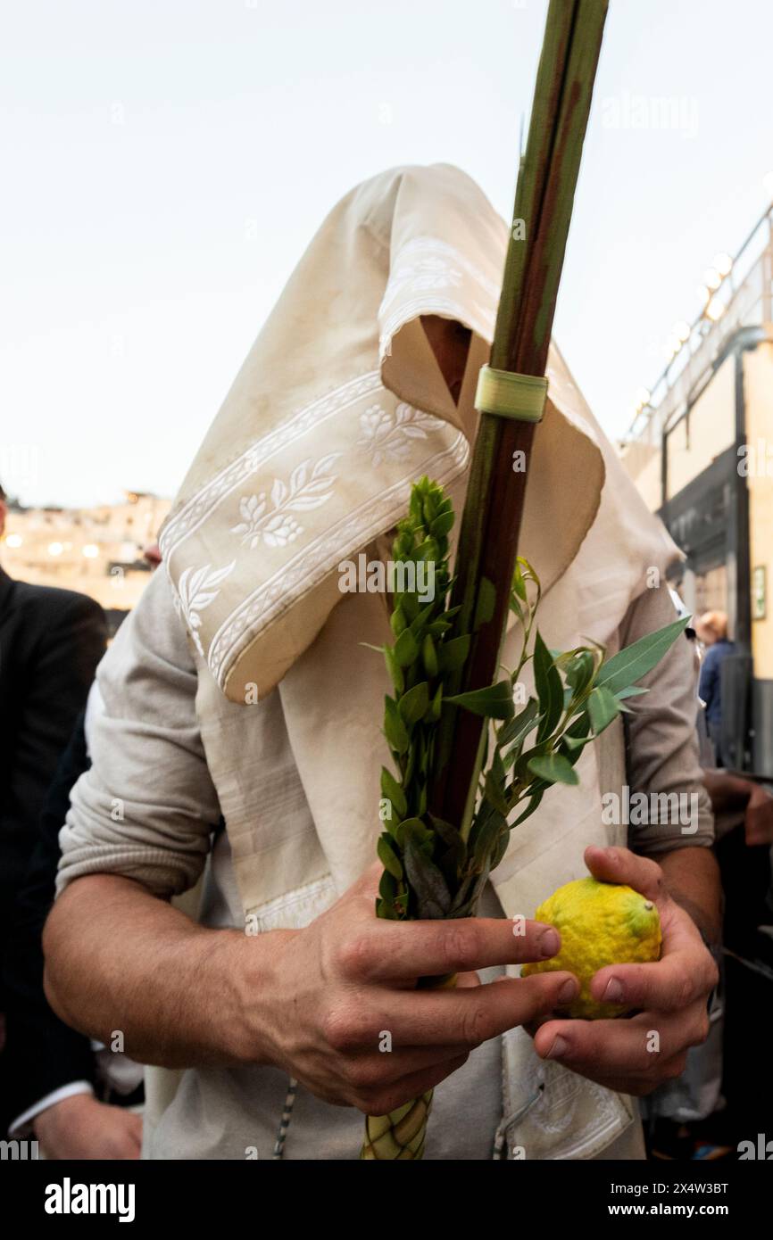An Orthodox Jewish man wearing a white tallit or prayer shawl holds a lulav and etrog or citron during prayer services on the festival of Sukkot at th Stock Photo