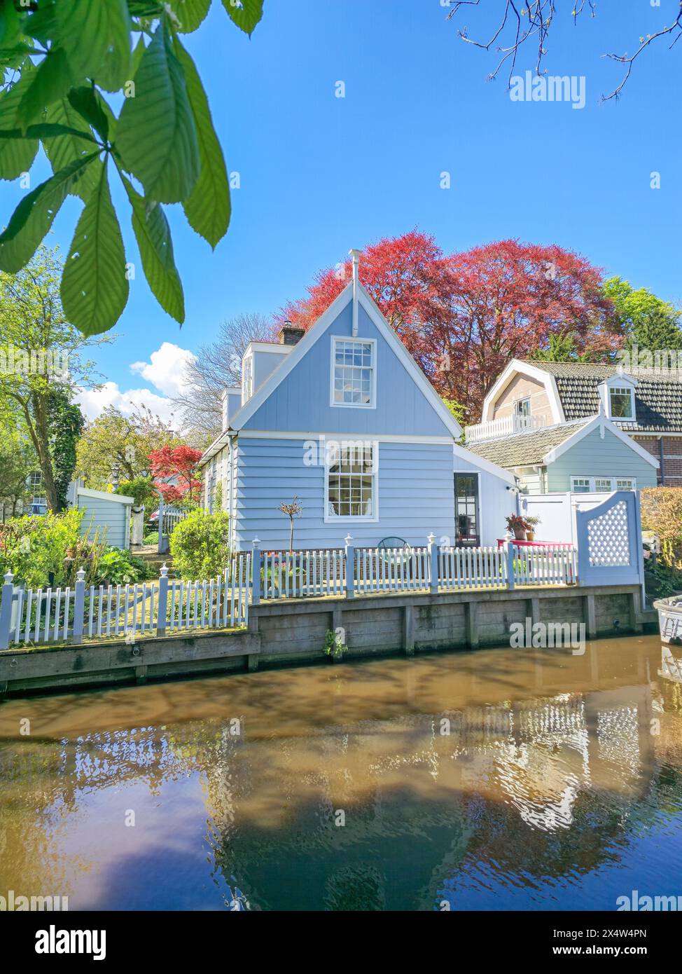 A charming blue house peacefully rests on the riverbank, surrounded by the tranquil waters and serene natural beauty. Broek in Waterland Netherlands  Stock Photo