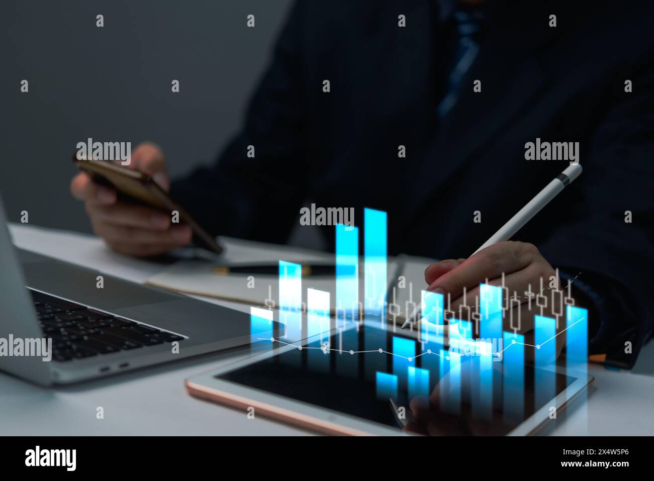 A business analysis examines interactive data charts on a tablet while simultaneously using a smartphone. Stock Photo