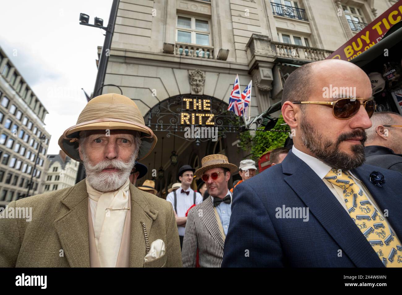 London, UK.  5 May 2024.  Elegantly dressed people pass The Ritz hotel during the fourth Grand Flâneur walk. Starting at the Beau Brummell statue on Jermyn Street, the walk coincides with the 25th anniversary of The Chap magazine and is defined as a walk without purpose, celebrating the art of the flâneur, oblivious to going anywhere specific, and an antidote to the demands of modern life and the digital smartphone.  Credit: Stephen Chung / Alamy Live News Stock Photo