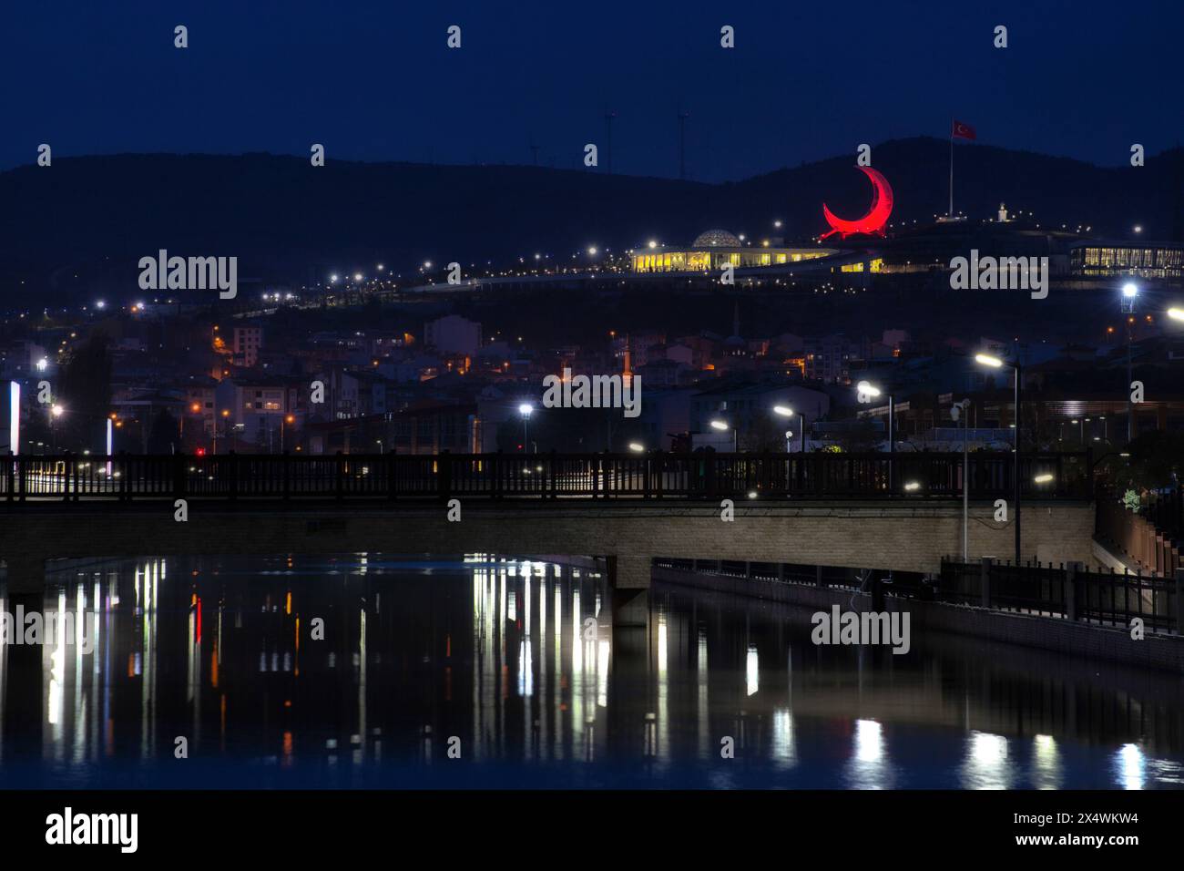 Night Scene of a bridge constructed over a water channel and a red moon shaped structure Stock Photo