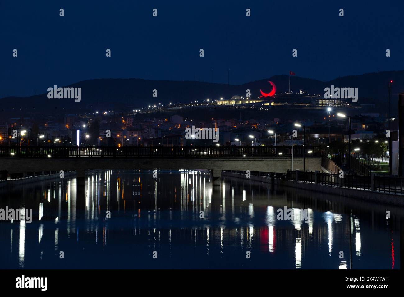 Night Scene of a bridge constructed over a water channel and a red moon shaped structure Stock Photo