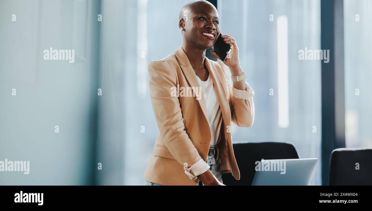 Successful African businesswoman in her office, using a smartphone and discussing business on the phone. She is professional and focused. Stock Photo