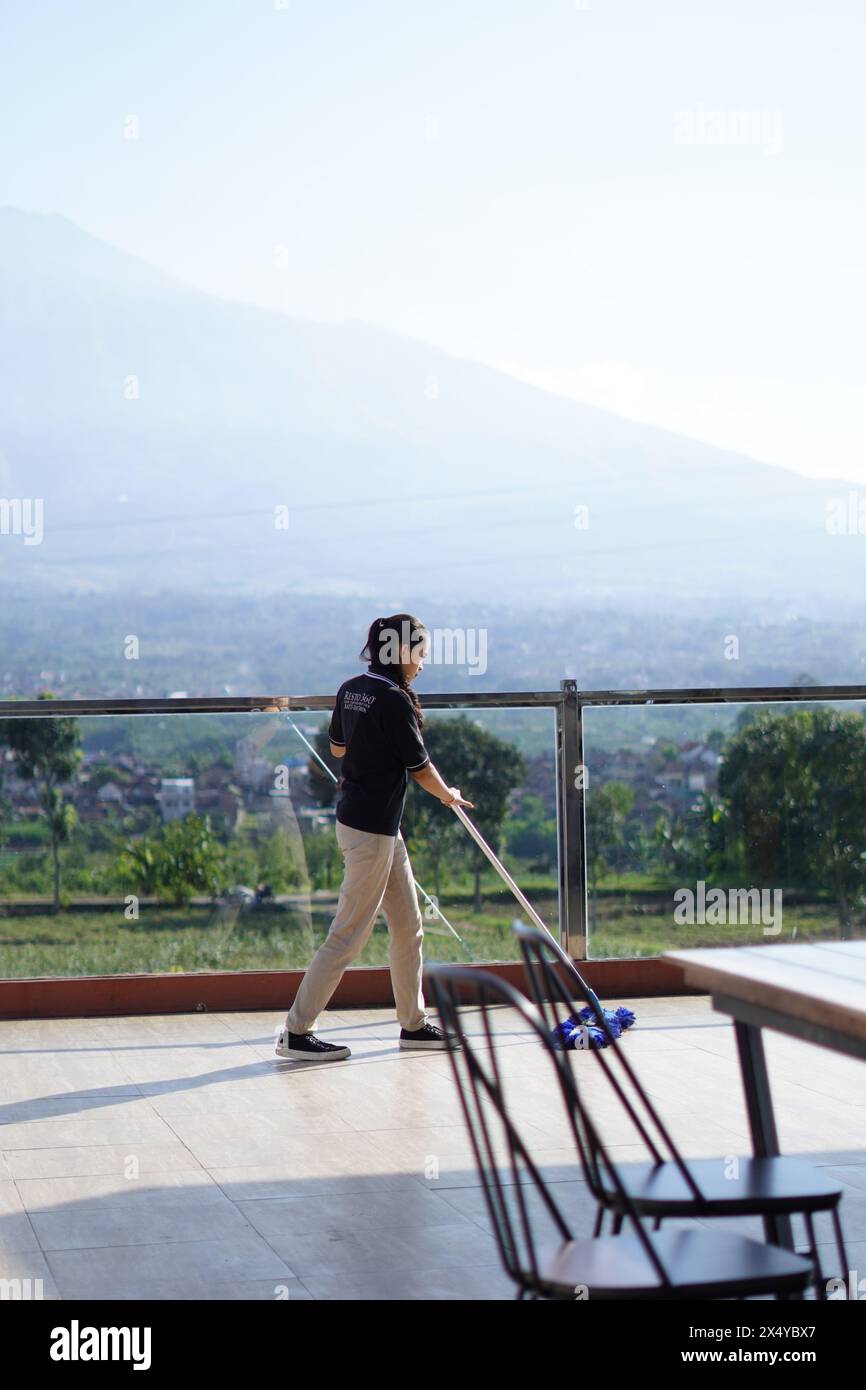 A woman mopping the floor of a restaurant in the morning with mountains in the background Stock Photo