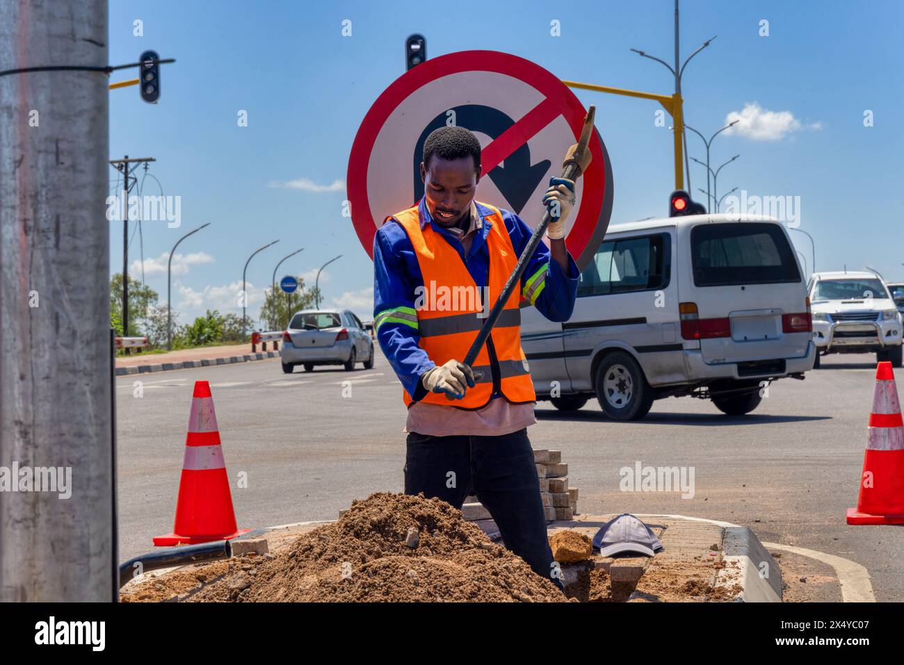 african american worker with a pickaxe digging a ditch in the highway to repair cabling on an isle at an intersection Stock Photo