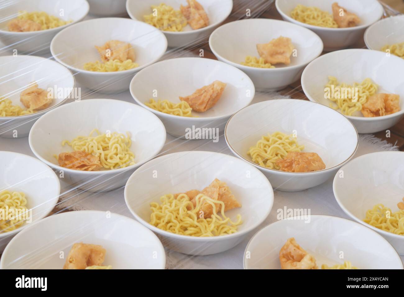 Several white bowls containing yellow noodles, fried foods and meatballs without sauce on the table Stock Photo