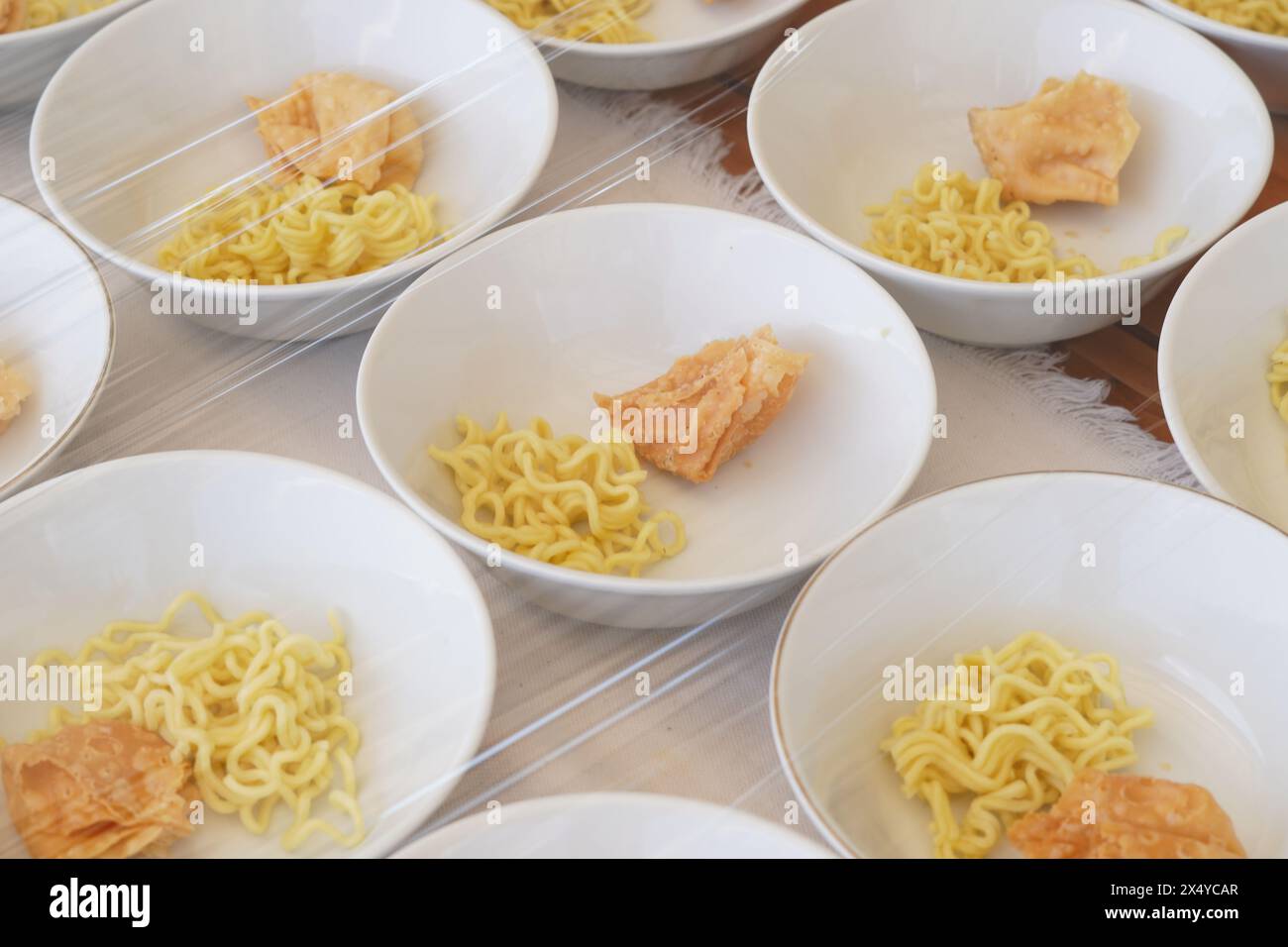 Several white bowls containing yellow noodles, fried foods and meatballs without sauce on the table Stock Photo