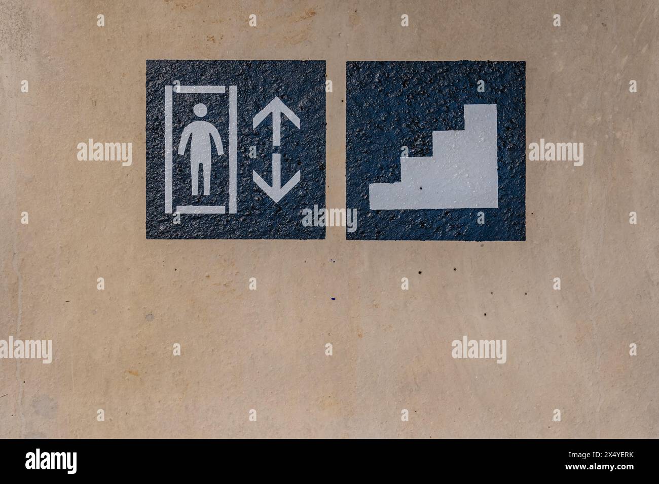 Close-up photo of a painted elevator and stairs sign on a concrete wall within a parking garage, car park. Stock Photo