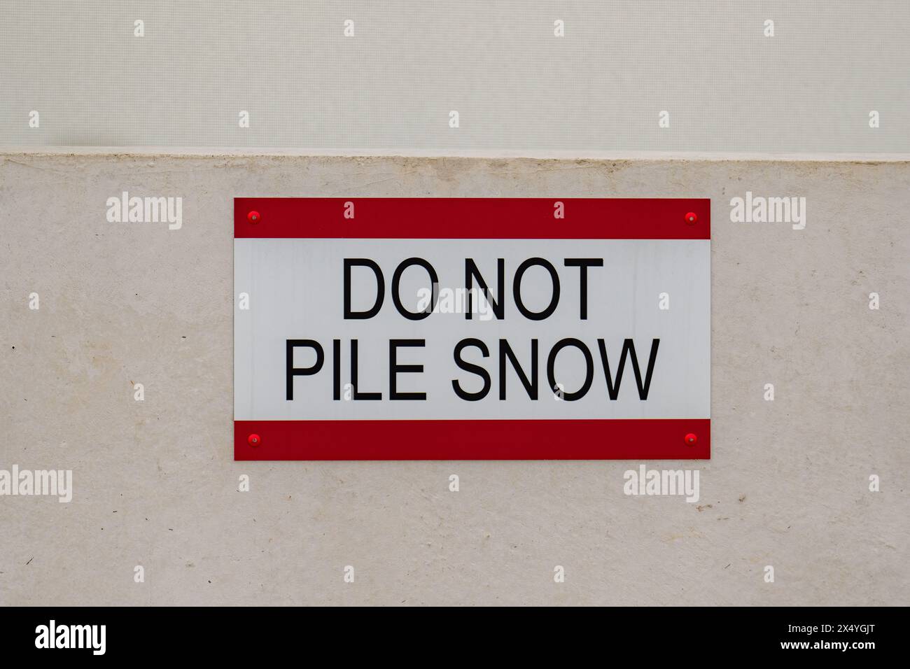 Close-Up photos of a DO NOT PILE SNOW sign on the roof of a concrete parking structure. Stock Photo