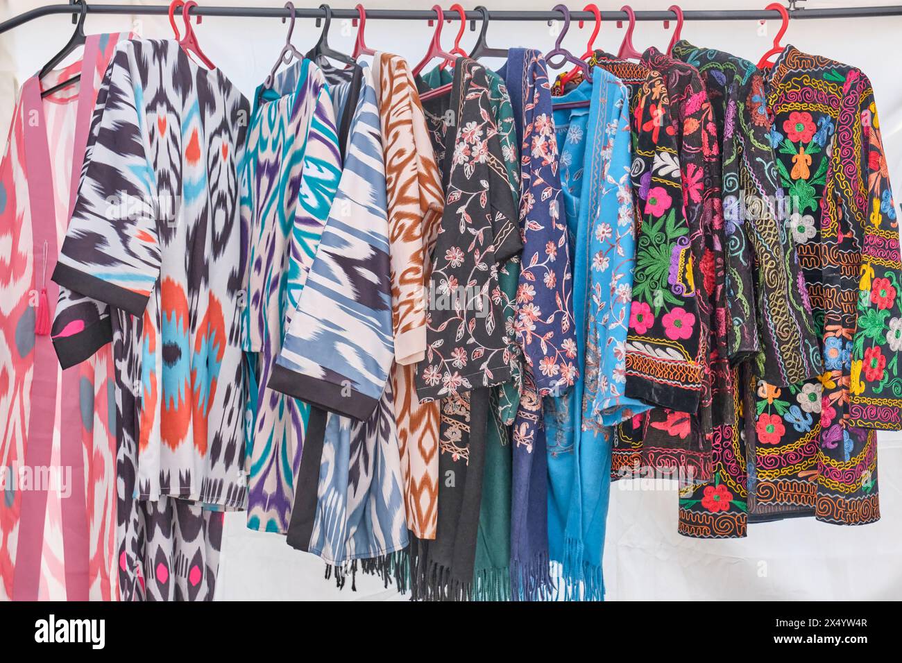 Women's Central Asian robes with traditional patterns and colorful embroidery on hangers in a row in a sales tent. Crafts fair on a pedestrian street, Stock Photo