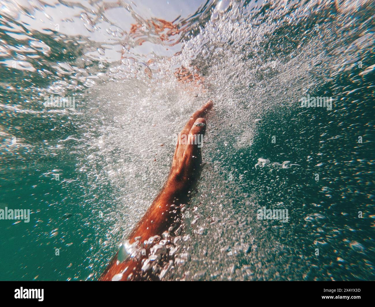 Man drowning in deep blue sea, close up of hand reaching to the ocean surface, surrounded with air bubble, swimmer fighting for his life, selective fo Stock Photo