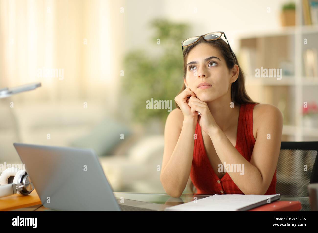 Serious student with a laptop thinking looking above at home Stock Photo