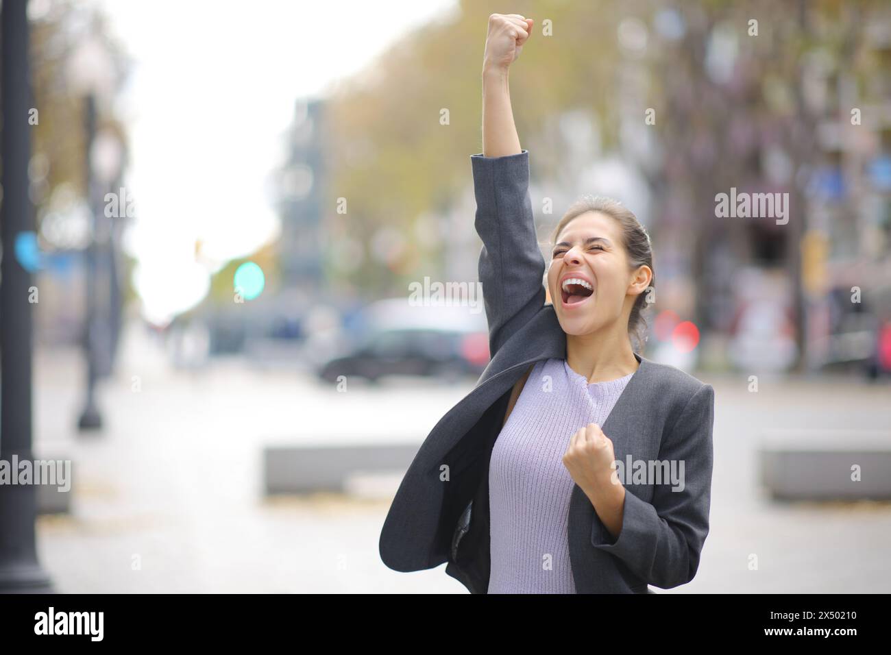 Excited businesswoman celebrating in the street raising arm and screaming Stock Photo