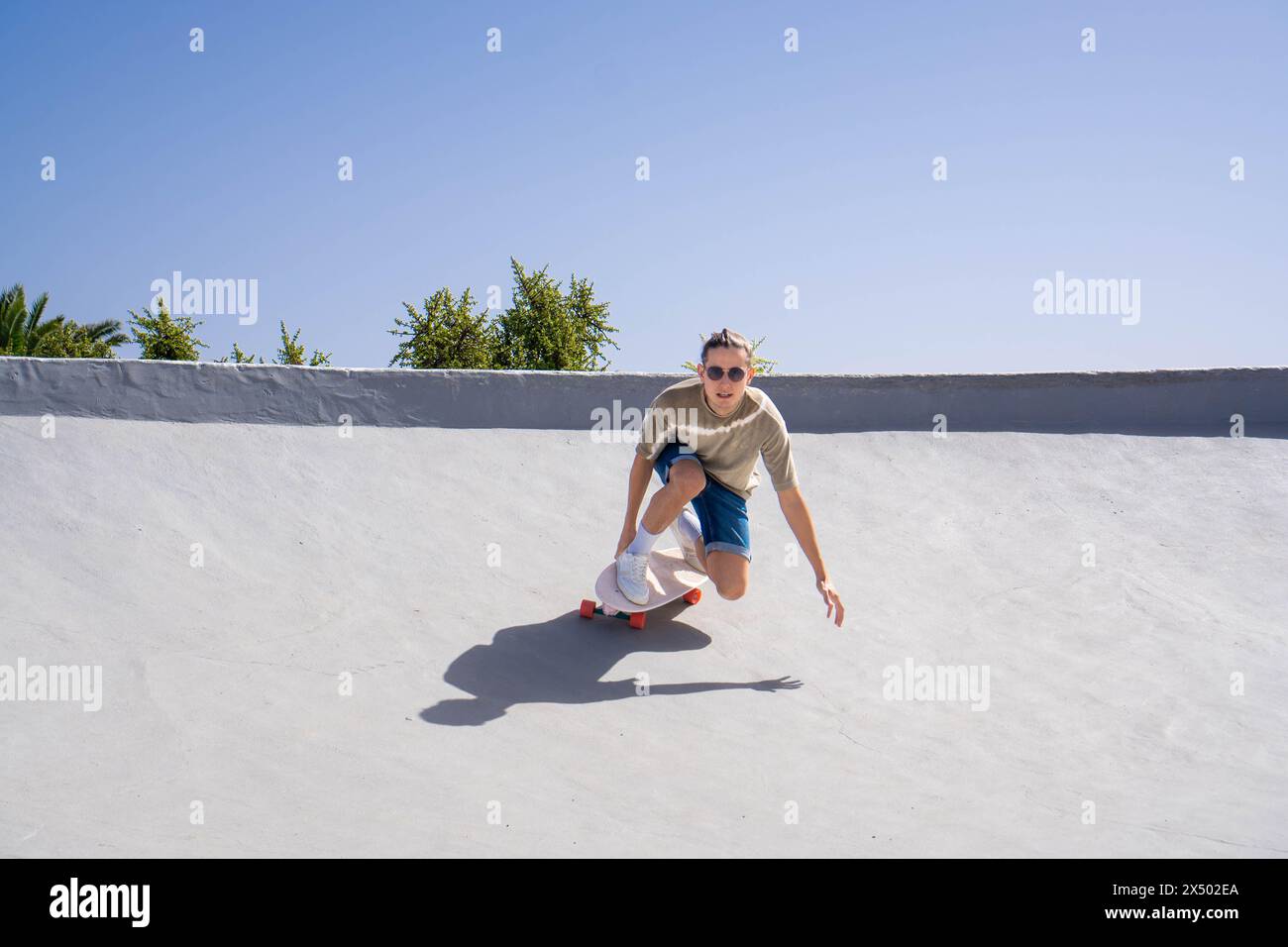 A young man is skillfully riding a skateboard down a cement ramp with a surfskate, showcasing his impressive skating abilities. Stock Photo